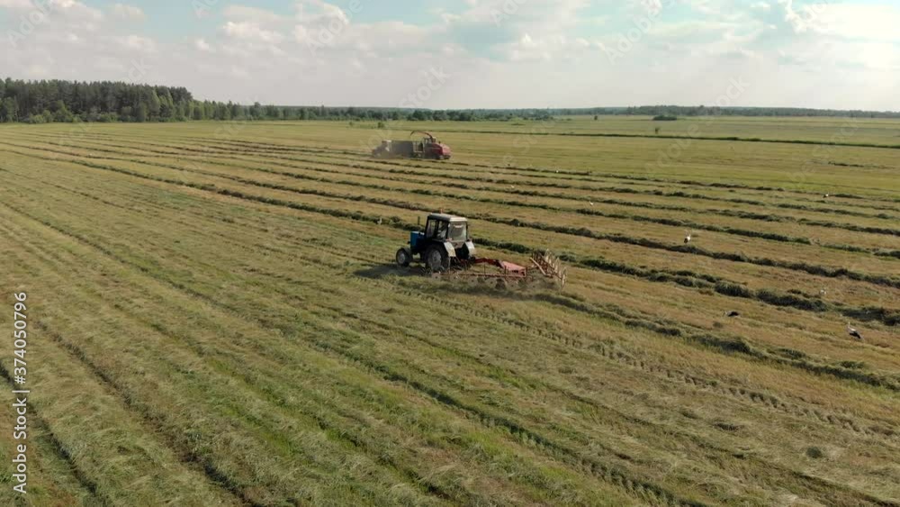 Aerial view of a green summer meadow with several tractors mowing and harvesting fresh grass for animal feed. Picturesque landscape with the working of agricultural machinery. Modern agribusiness Aerial view of a green summer meadow with several tractors mowing and harvesting fresh grass for animal feed. Picturesque landscape with the working of agricultural machinery. Modern agribusiness