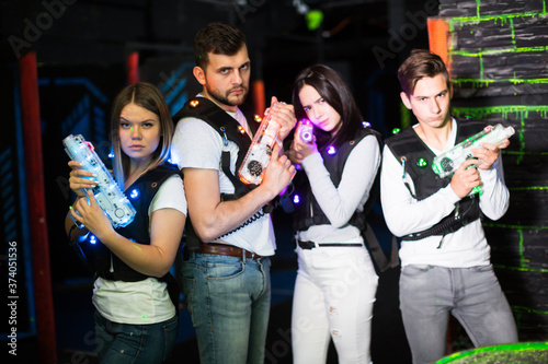Portrait of cheerful young friends with laser guns during lasertag game in dark room.