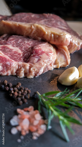 fresh slices of raw meat steak pork beef on black slate stone plate background with ingredients spices salt pepper garlic rosemary preparing and marinating barbecue meat. Healthy, natural food.