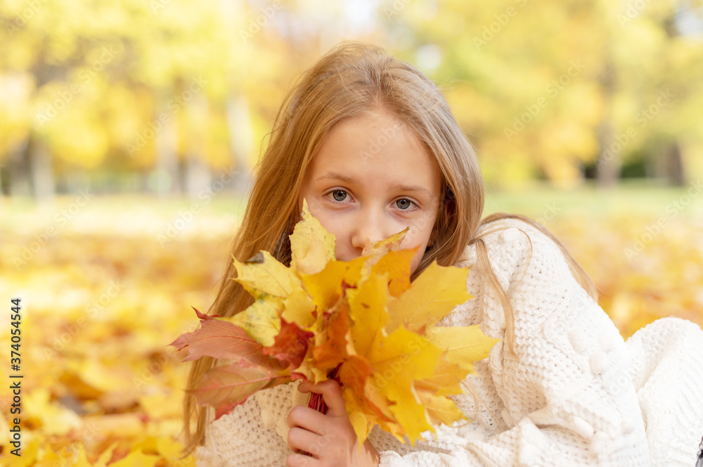 beautiful blonde teen girl sitting on the grass in an autumn Park with maple trees beautiful blonde teen girl sitting on the grass in an autumn Park with maple trees