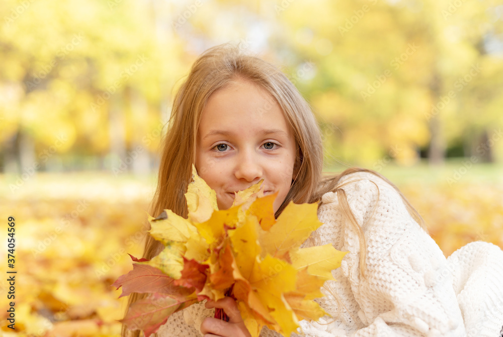beautiful blonde teen girl sitting on the grass in an autumn Park with maple trees beautiful blonde teen girl sitting on the grass in an autumn Park with maple trees