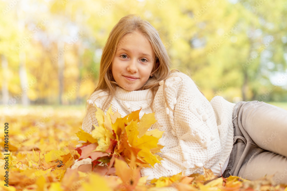 beautiful blonde teen girl sitting on the grass in an autumn Park with maple trees beautiful blonde teen girl sitting on the grass in an autumn Park with maple trees