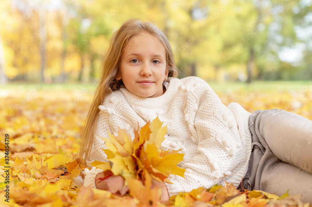 beautiful blonde teen girl sitting on the grass in an autumn Park with maple trees beautiful blonde teen girl sitting on the grass in an autumn Park with maple trees