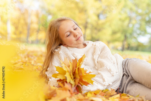 beautiful blonde teen girl sitting on the grass in an autumn Park with maple trees