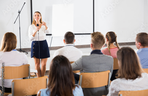 Confident female student answering with microphone in front of student group in auditorium