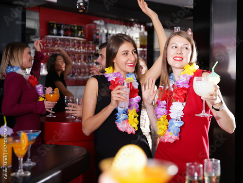 Happy young female colleagues enjoying company party in Hawaiian style in bar