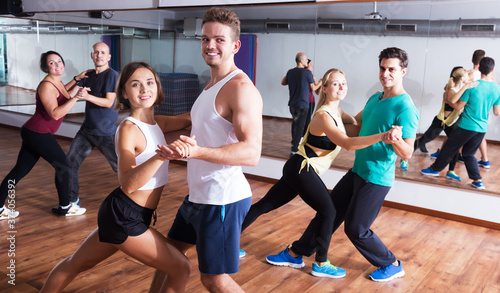 Group of young cheerful people learning salsa at dance class