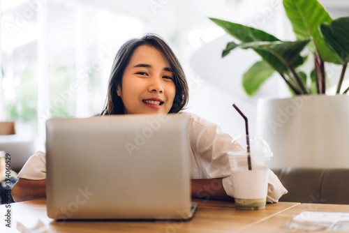 Portrait of smiling happy beautiful asian woman relaxing using laptop computer while sitting on sofa.Young hipster girl freelancer working and thinking with new ideas in cafe and restaurant