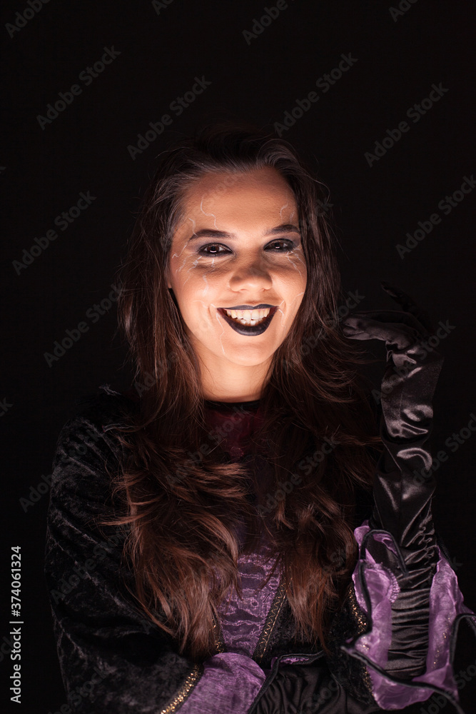 Beautiful woman dressed up like a witch having a scary smile over black background.