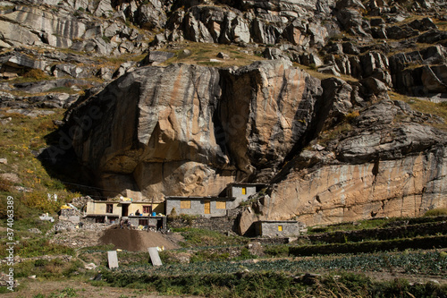 Rooms under huge boulders in Spiti Valley with some people and yellow doors and windows.