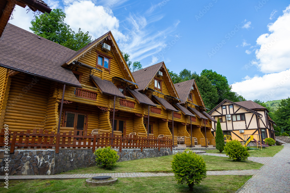 Modern wooden houses from a felling on a background of mountains. Wooden houses with landscaped area on a background of mountains. Traditional wooden cottages at sunny day. Modern wooden houses from a felling on a background of mountains. Wooden houses with landscaped area on a background of mountains. Traditional wooden cottages at sunny day.