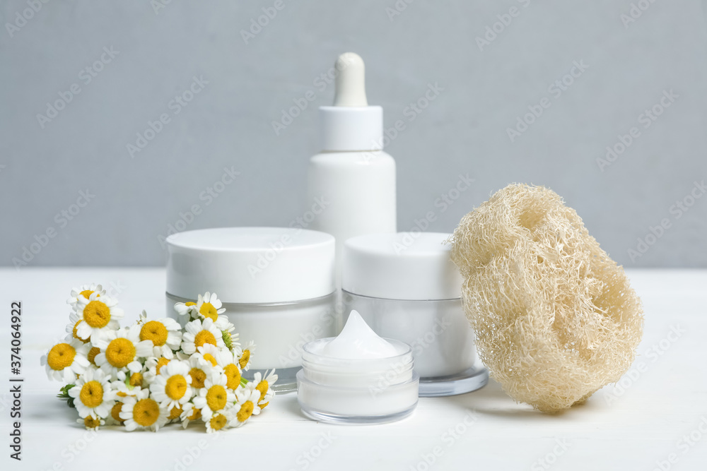 Set of cosmetic products, chamomiles and loofah on white table against grey background Set of cosmetic products, chamomiles and loofah on white table against grey background