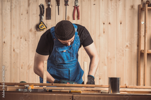 Home repair concepts, close up. Handicraft Carpentry. Cabinet-maker hands drilling a wooden plank using screwdriver on the working table in the workshop