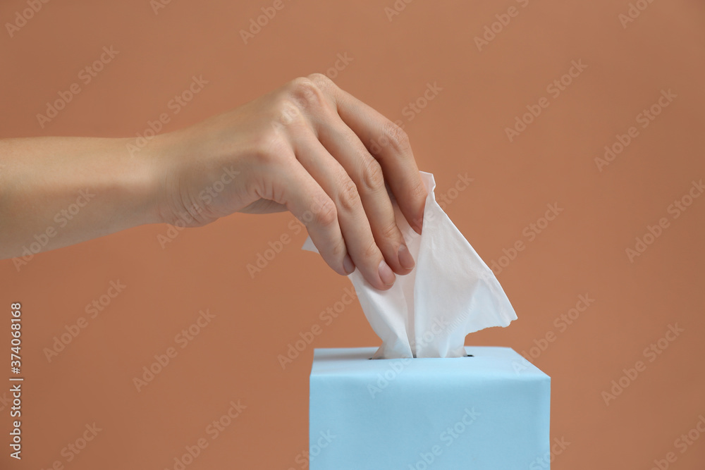 Woman taking paper tissue from box on light brown background, closeup Woman taking paper tissue from box on light brown background, closeup