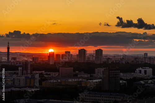 Black silhouettes of buildings are on a red sky background with orange and yellow sunset