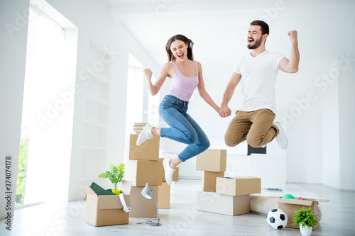 Full length body size view of nice attractive cheerful cheery overjoyed lucky couple jumping rejoicing purchase real-estate property having fun lottery winner at light white interior house indoors