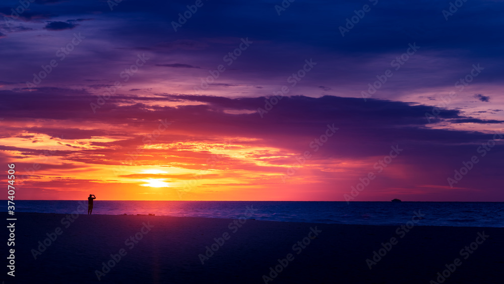 Silhouette of man taking photos of dramatic cloudscape at sunrise over ocean