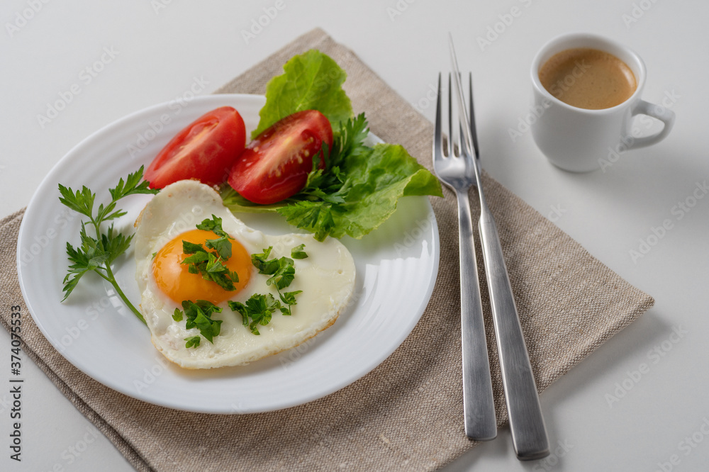 Healthy and hearty breakfast. Close-up of a fried eggs, tomato, herbs and espresso coffee. Served on a white table with a linen napkin and cutlery.