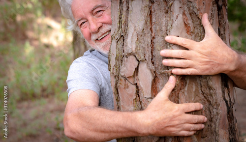 Blurry human hands hugging a tree trunk in the woods - love for nature, earth day concept. An old man hiding behind the trunk. People save the planet from deforestation