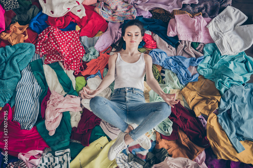 High angle above view photo of pretty focused lady stay home quarantine spring cleaning household lying many clothes heap stack floor prepared untidy dirty stuff resting meditating indoors photo