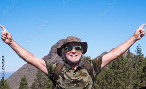 Happy senior man with raised arms traveling in mountain landscape in Tenerife, smiling and enjoying freedom - horizon over the sea - active retired elderly and fun concept