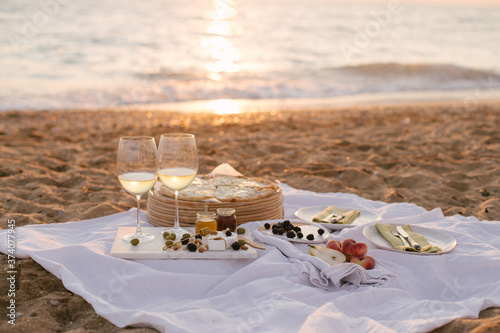 Summer picnic at sunset on beach with white wine, pizza, cheese, olives and fresh fruits.