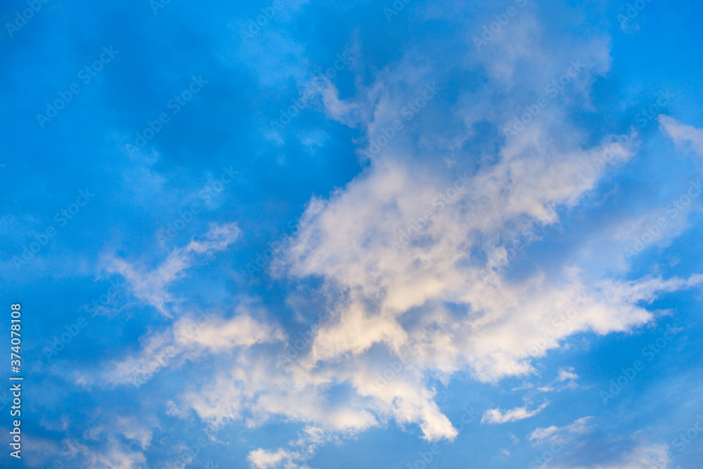 White clouds in the blue sky are highlighted by the setting sun. Evening sky