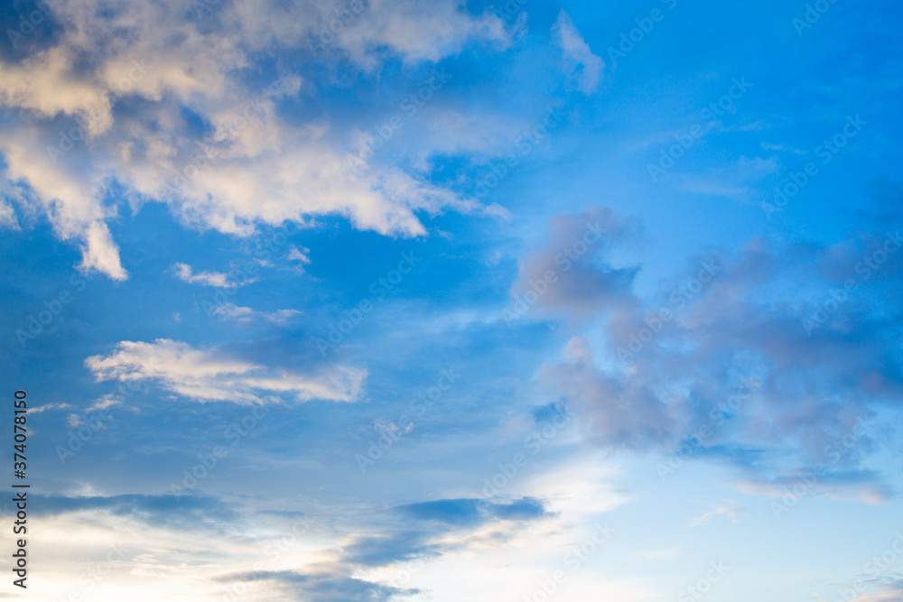White clouds in the blue sky are highlighted by the setting sun. Evening sky White clouds in the blue sky are highlighted by the setting sun. Evening sky