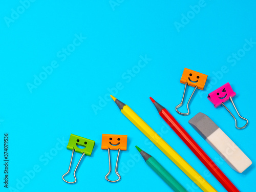 Smiles Binder Clips with Yellow, Green and Red Pencils on Blue Background. Office supplies on table. Education concept. Back to school. Eraser or rubber