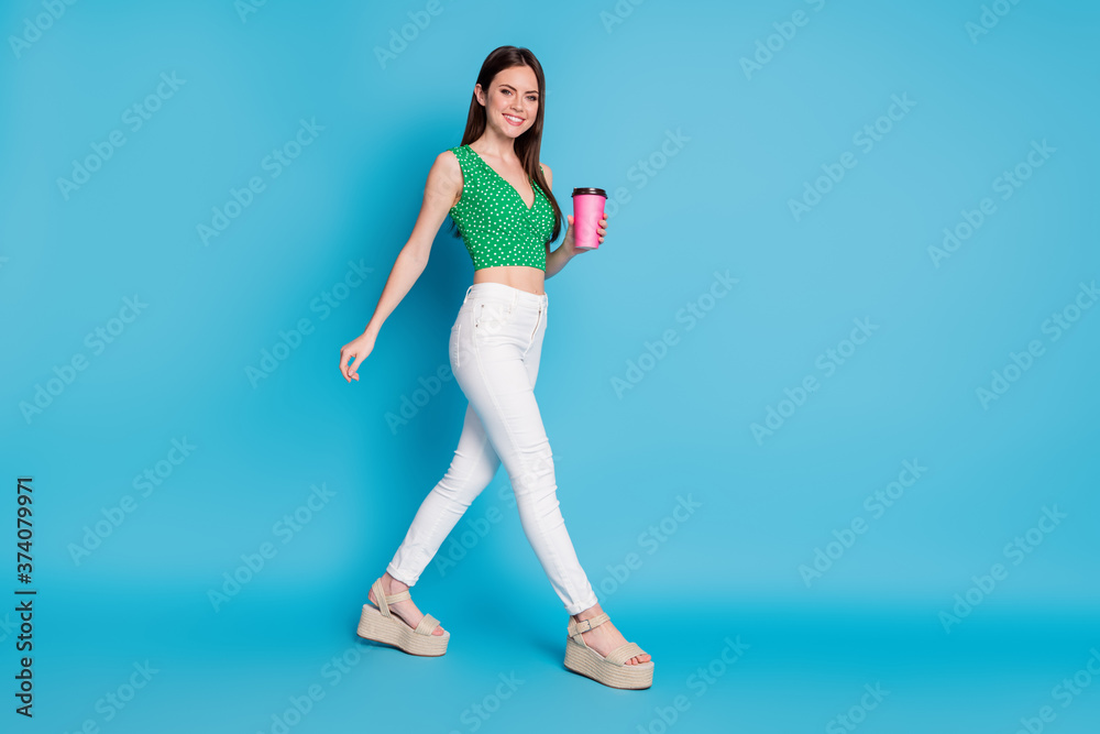 Full length profile side photo of positive cheerful girl hold coffee takeout cup have free time walk copyspace wear singlet sandals isolated over blue color background
