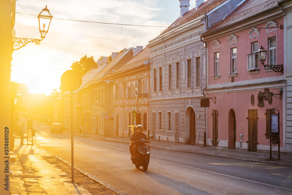 August 2020, Serbia, Novi Sad, Petrovaradin. A couple on a motorcycle rides through the old city at sunset. Travel to the Balkans - obrazy, fototapety, plakaty 