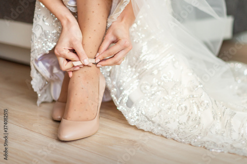 Bride puts on wedding shoes on her feet wearing beautiful wedding dress