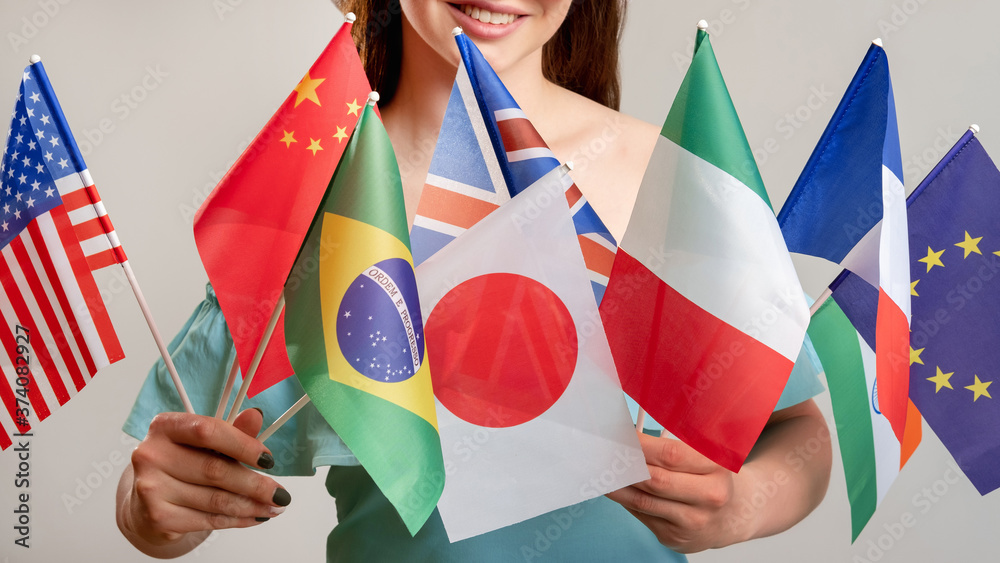 Global travel. Diplomatic relationship. Happy woman holding many international hand flags isolated on neutral. Visa office. Ethnic friendship. Exchange students
