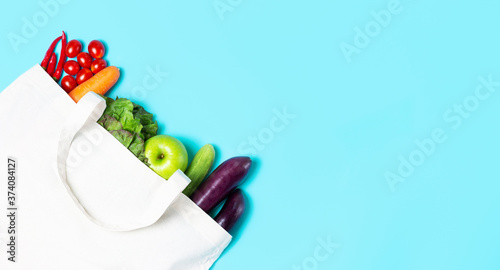 Multicolored vegetables and fruits in white linen bag on blue background.
