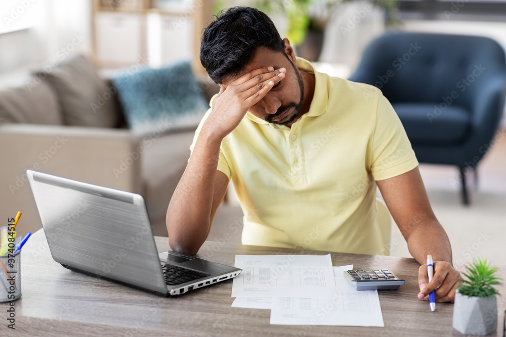 remote job, technology and people concept - stressed young indian man with calculator and papers working at home office remote job, technology and people concept - stressed young indian man with calculator and papers working at home office