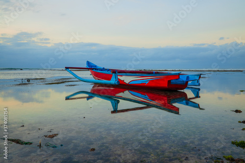 Seascape. Fisherman boat jukung. Traditional fishing boat at the beach during sunset. Cloudy sky. Water reflection. Thomas beach, Bali