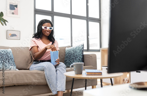 people, race, ethnicity and portrait concept - happy smiling african american young woman in 3d glasses watching tv and eating popcorn at home
