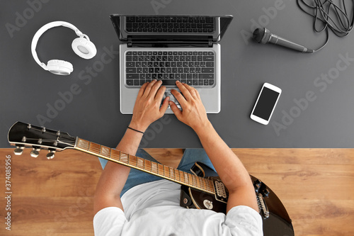 leisure, music and people concept - young man or musician with laptop computer and guitar sitting at table