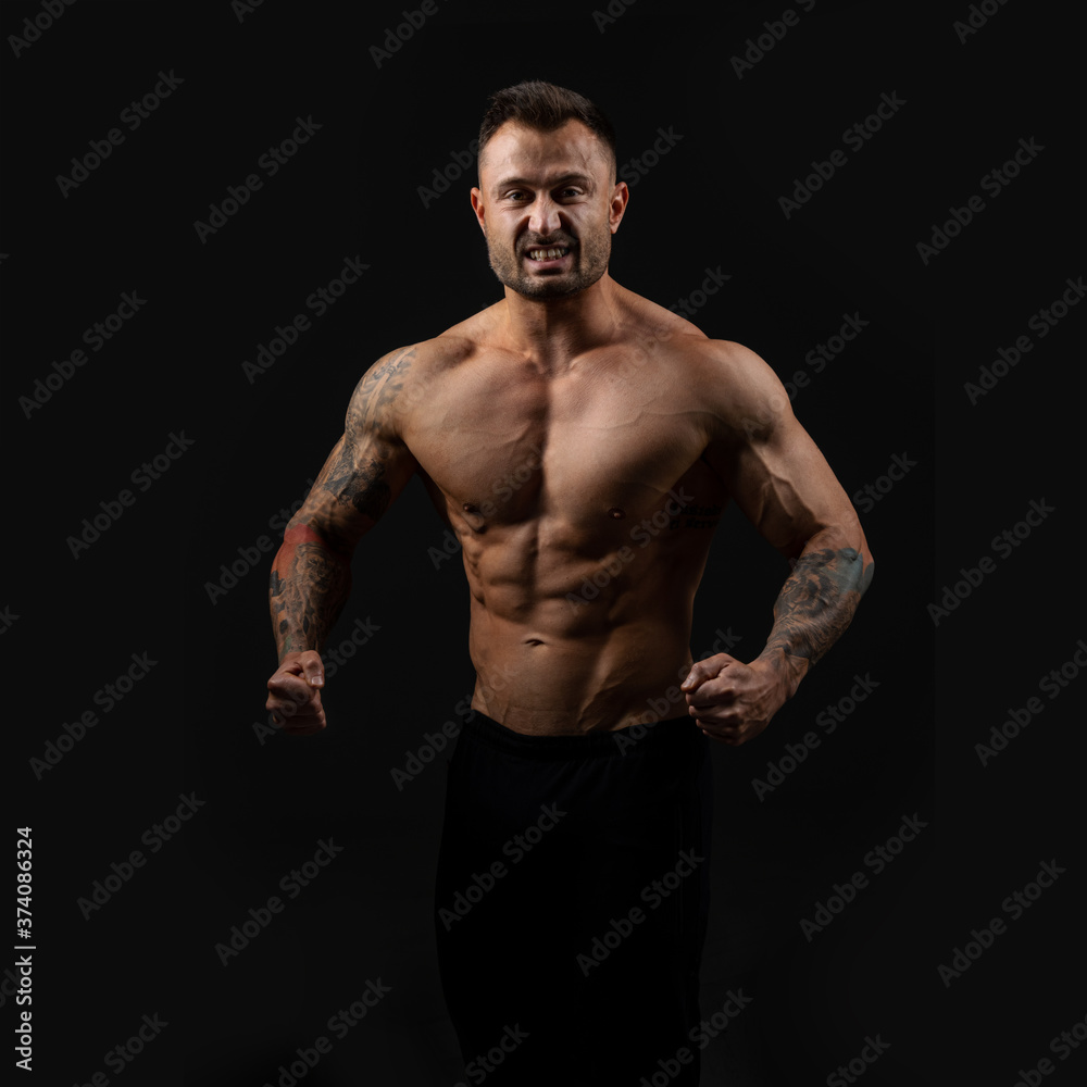 Handsome bodybuilder man with an ideal body, after coaching abdominal muscles, biceps, triceps on dark background.