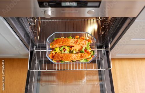 food, eating and culinary concept - salmon fish with vegetables cooking in baking dish in oven at home photo
