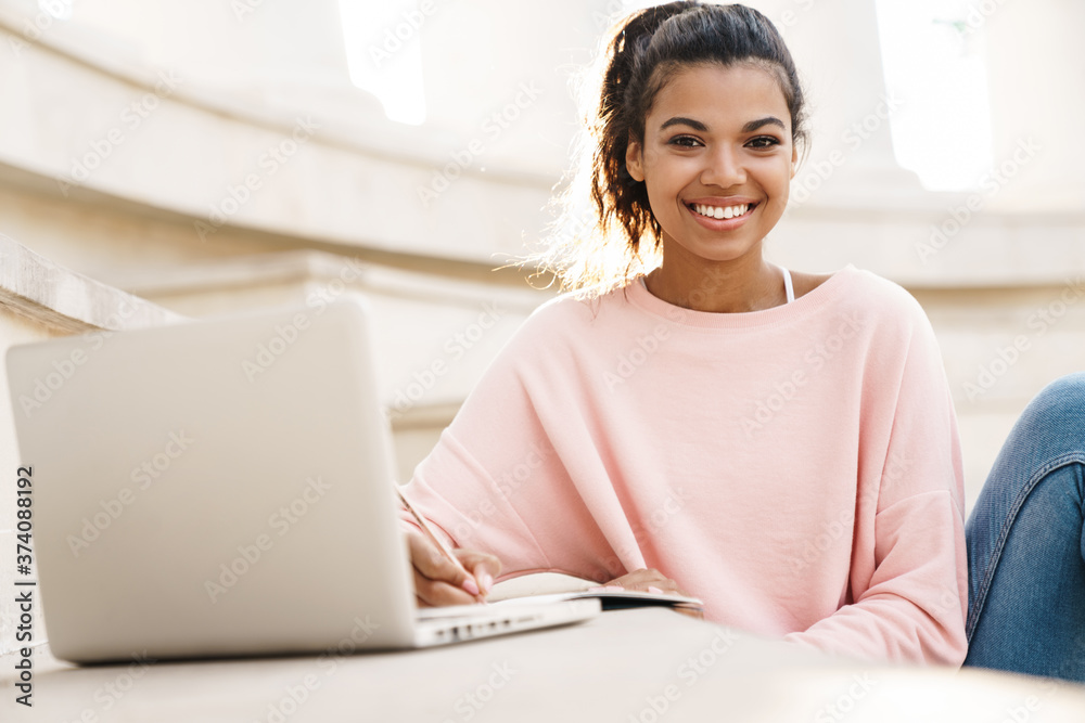 Image of cheerful african american student girl doing homework with laptop Image of cheerful african american student girl doing homework with laptop