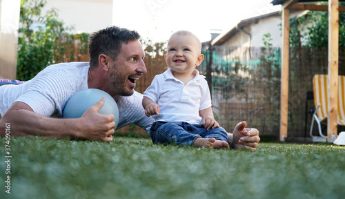 Fotografija A cute baby and his smiling father playing on a grass with a pilates ball