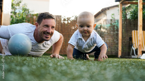 Fotografija A cute baby and his smiling father playing on a grass with a pilates ball