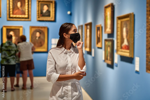 Fototapeta Woman visitor wearing an antivirus mask in the historical museum looking at pictures