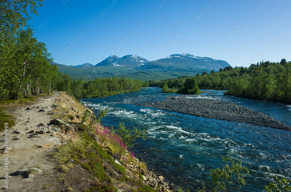 Nature of Scandinavia in summer. Hiking trail lays along Abiskojokk river in Abisko National Park in northern Sweden. Sunny day Nature of Scandinavia in summer. Hiking trail lays along Abiskojokk river in Abisko National Park in northern Sweden. Sunny day