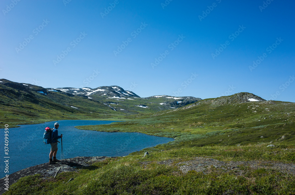 Hiking in Swedish Lapland. Man traveler trekking alone with view of mountain lake Allagasjavri in Sweden. Arctic nature of Scandinavia in warm summer sunny day with blue sky