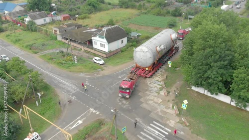 A truck driver with an oversized cargo on a trailer makes a turn on a narrow road, filmed from a drone, side view. Delivery and logistics of goods from different places, top view