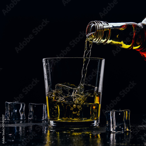 Whiskey pours from a bottle into a glass on a dark background