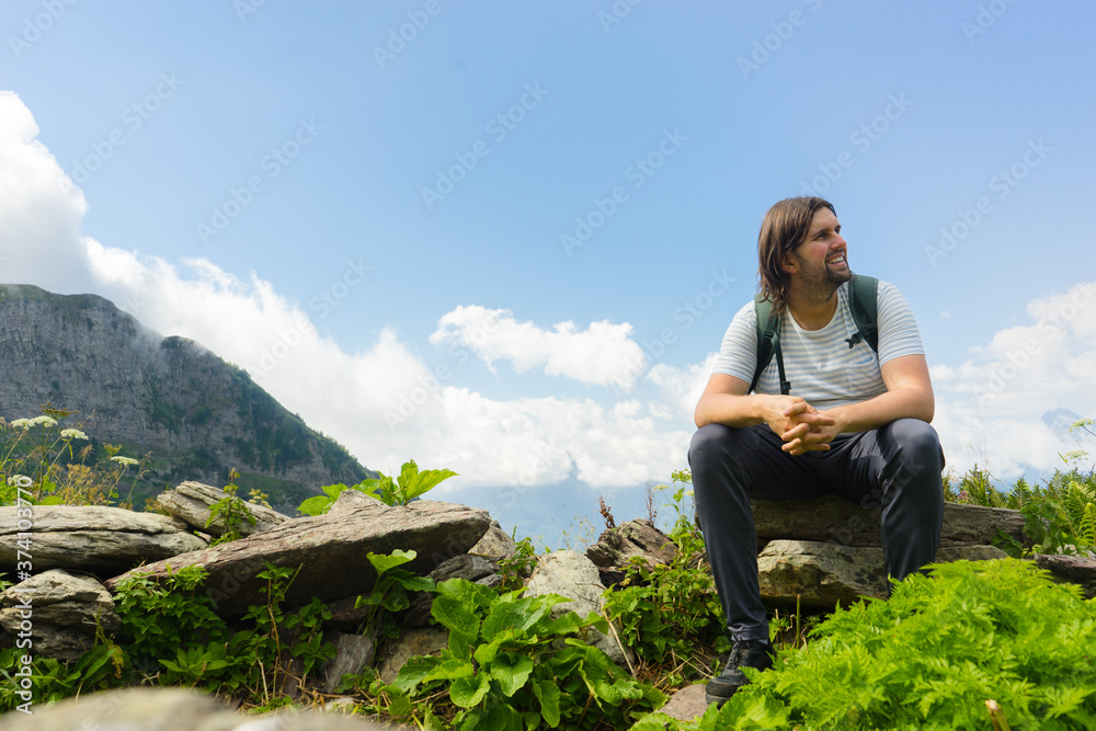 Young hiker sit in beautiful mountains on hiking trip. Active person resting outdoors in  nature. Backpacker camping outside recreation active
