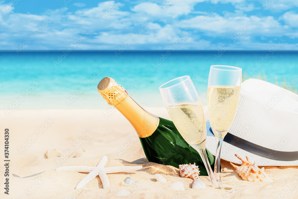Romantic sea beach. Wine glasses, a hat and a bottle of champagne on the background of snow-white sand with seashells, azure blue sea, ocean